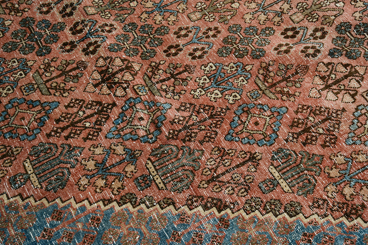 Close-up of antique Josheqan rug field with repeating geometric motifs in terracotta and blue tones