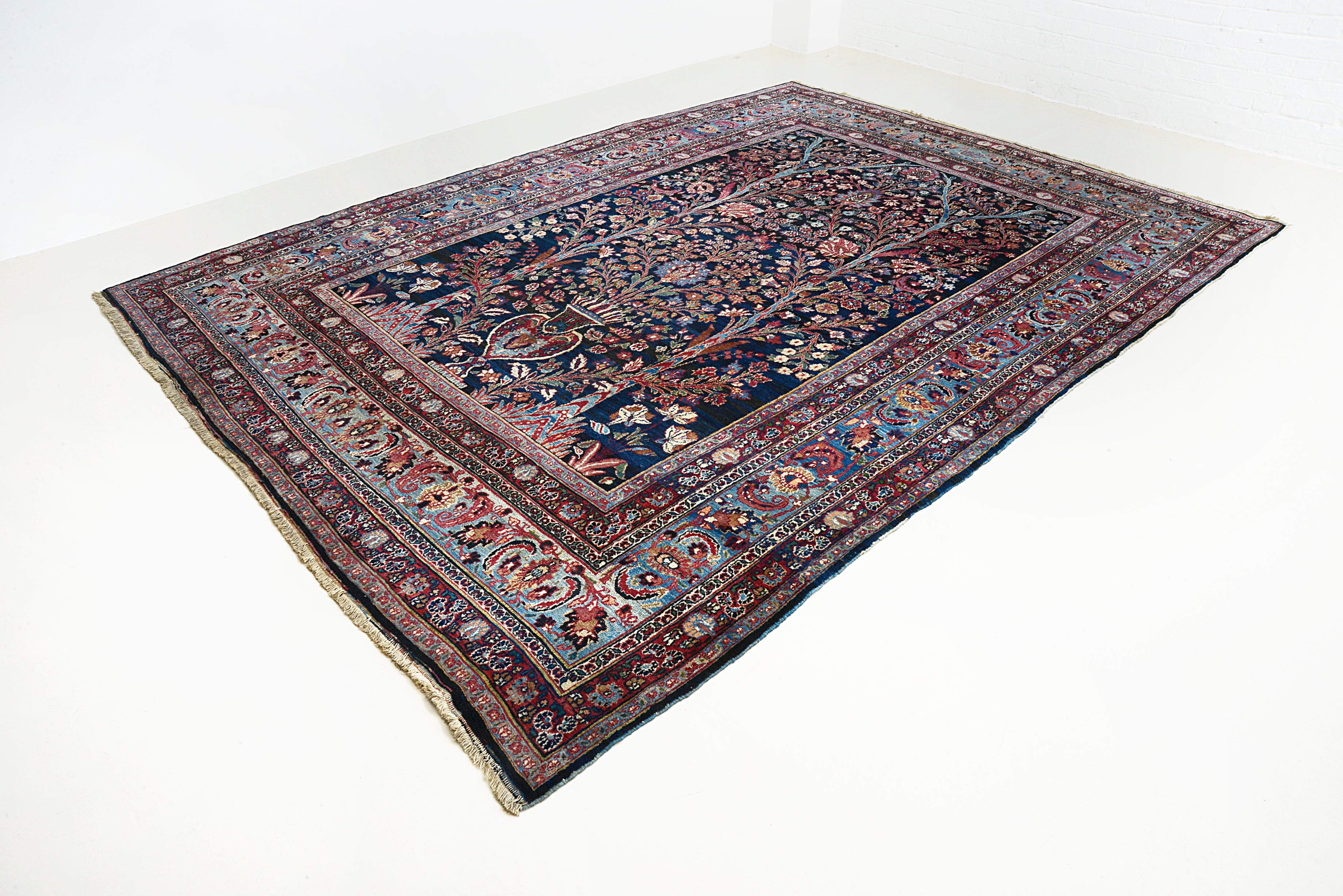 Angled view of an antique Persian Mashhad carpet highlighting its large scale and all-over floral design