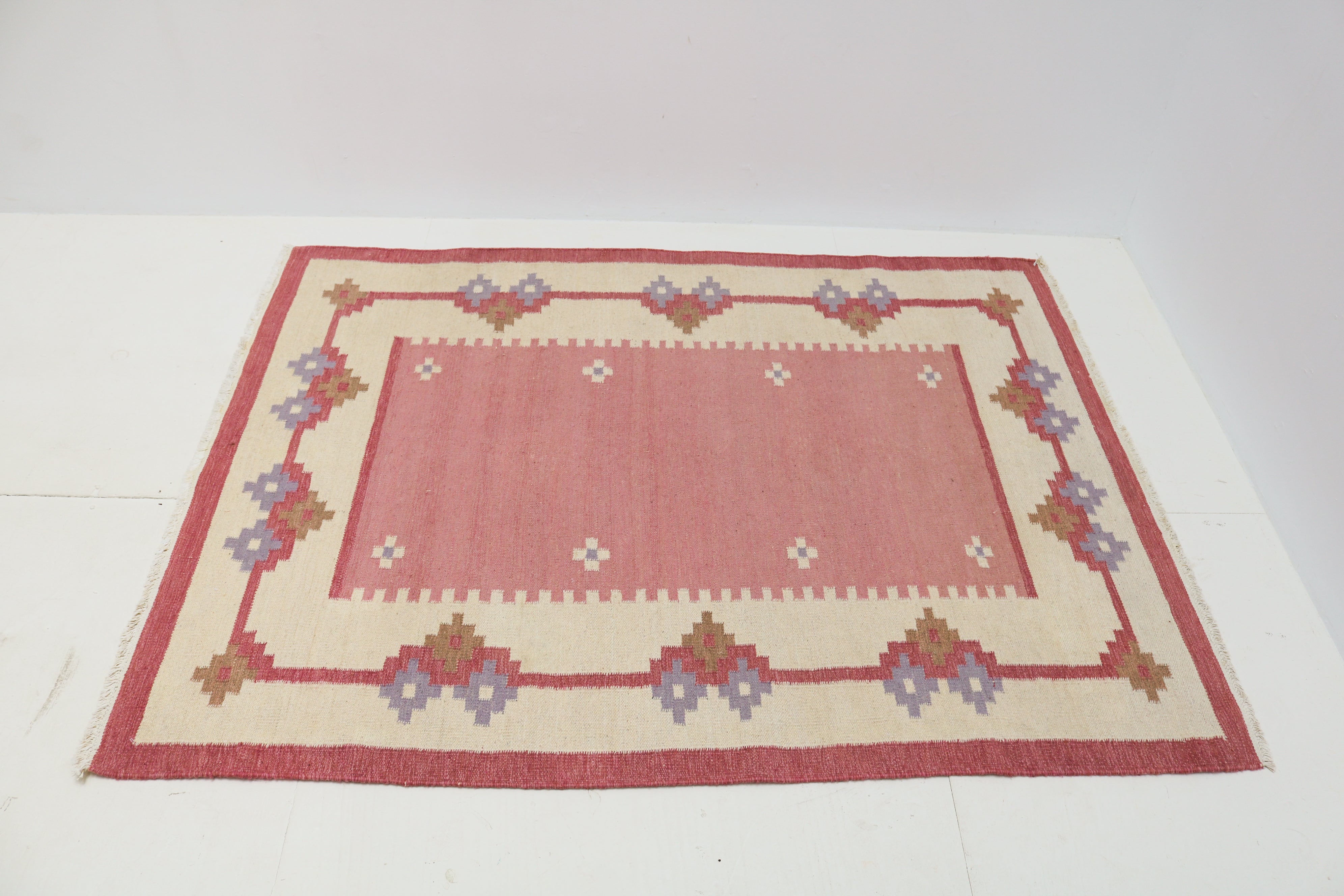 Handwoven Swedish flatweave rug with pink field and geometric border