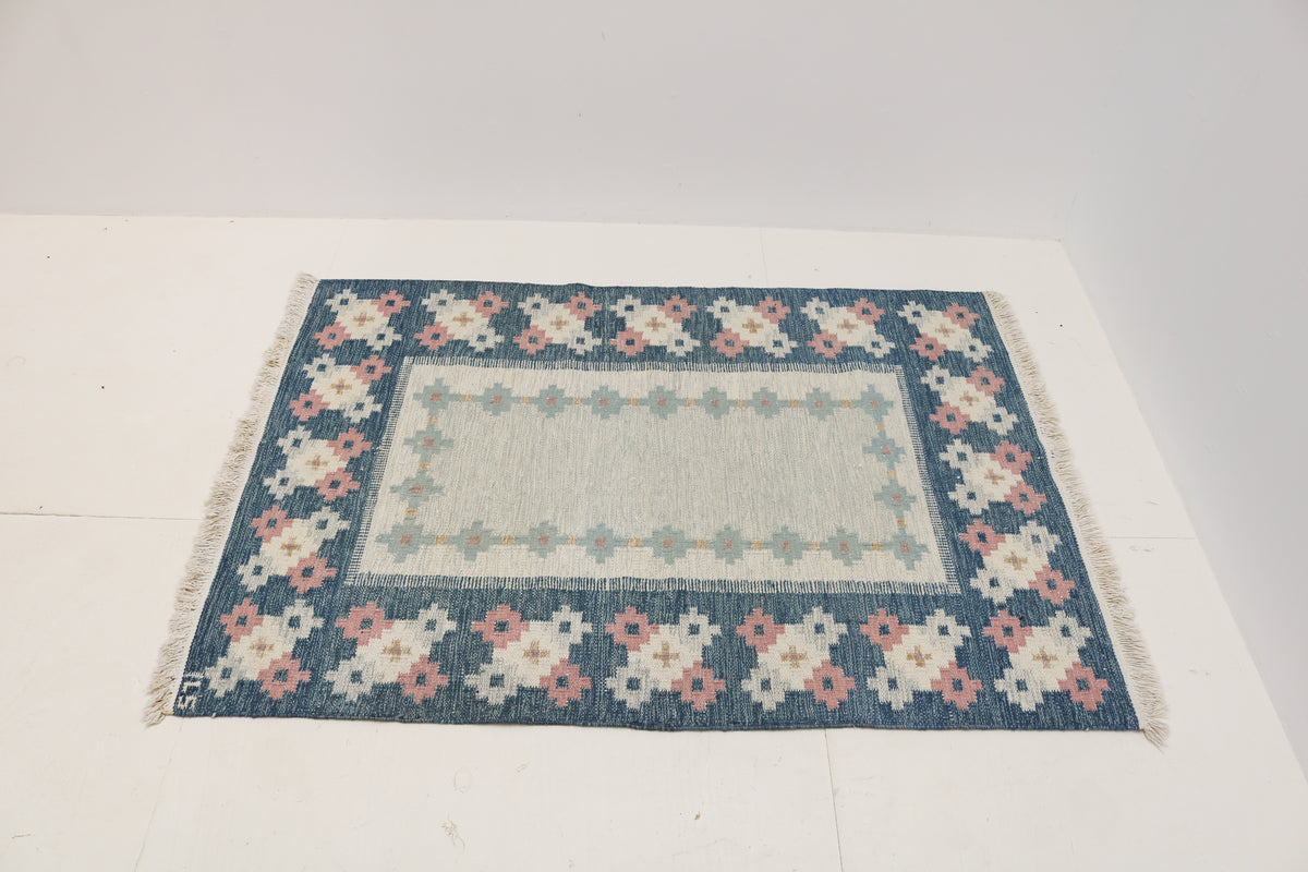 Angled view of Swedish Kilim rug featuring pale blue, ivory and dusty pink motifs