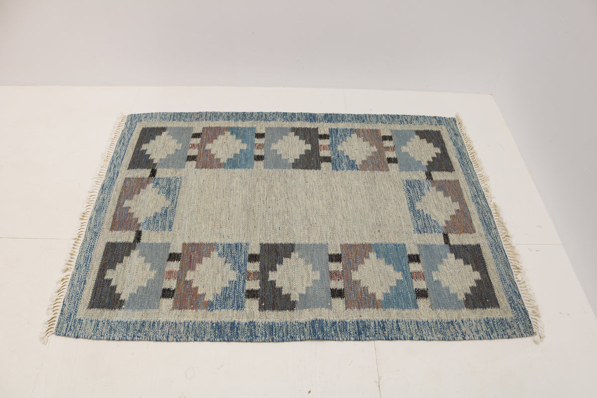 Angled view of Swedish Kilim rug featuring muted blue, ivory and charcoal medallions