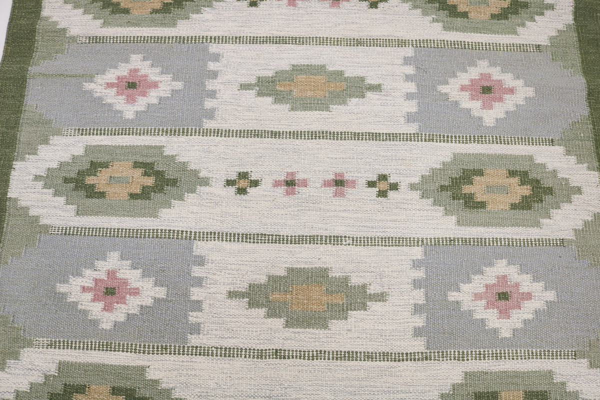 Detailed Swedish Kilim rug surface featuring repeating geometric motifs in ivory, green and dusty pink