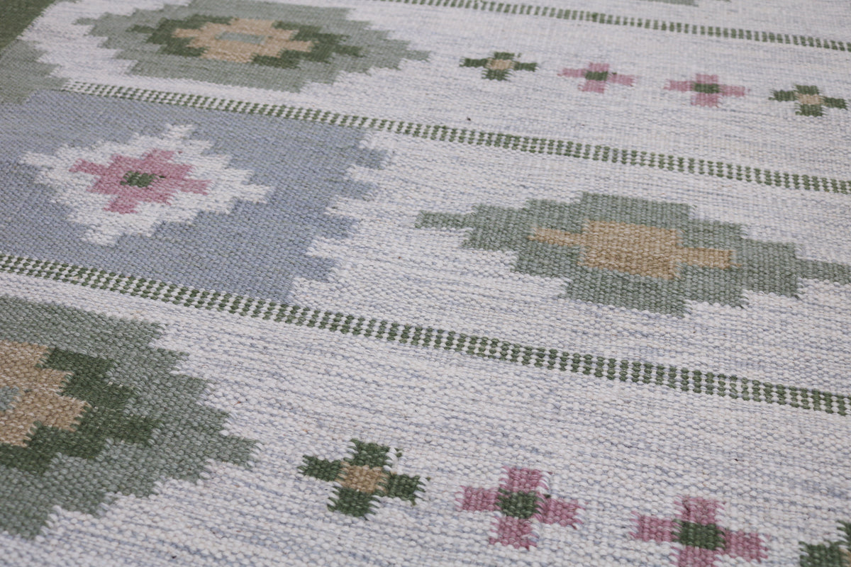 Close-up of Kilim rug with geometric floral motifs in muted green, pink and warm beige