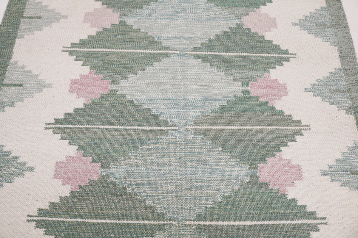 Detailed vintage Swedish Kilim rug surface with repeating diamonds in muted green and pink