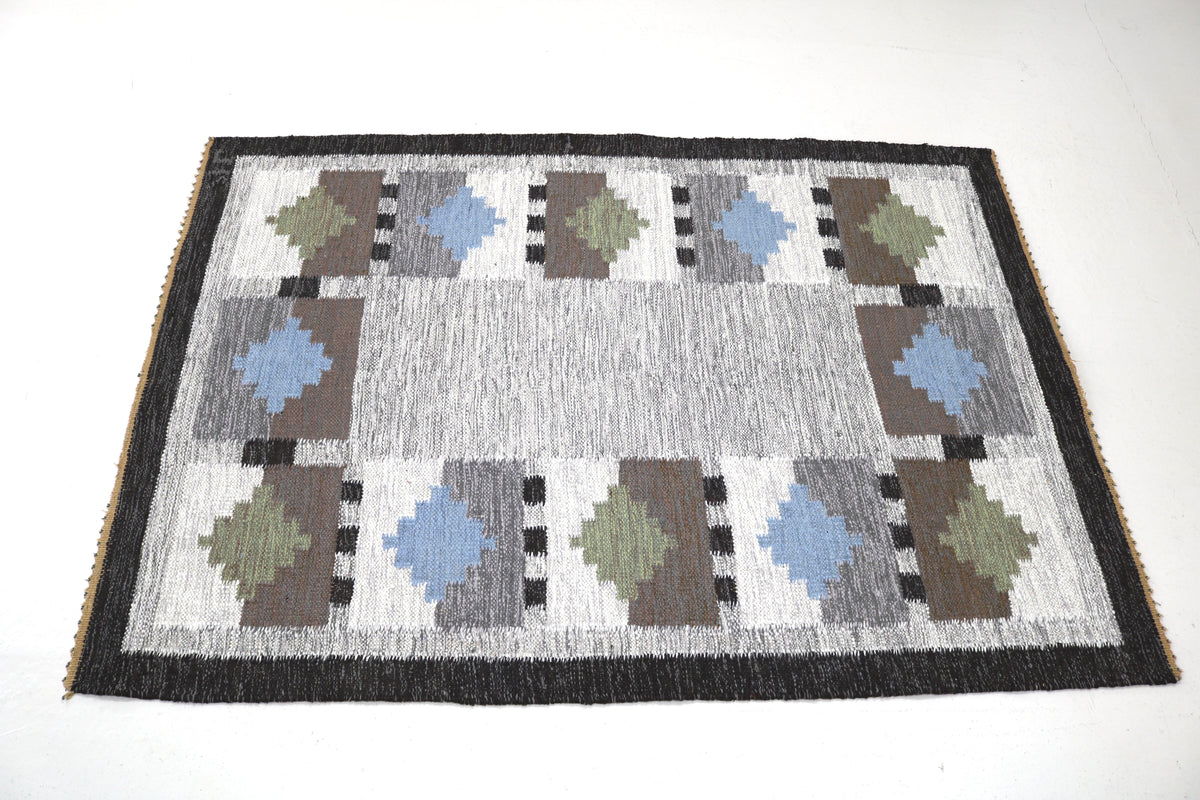 Angled view of Swedish Kilim rug featuring blue, olive, taupe and charcoal geometric motifs