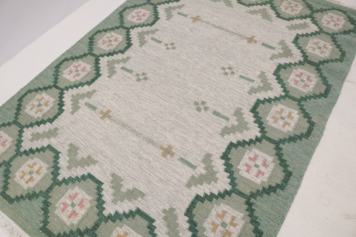 Angled view of vintage Swedish Kilim rug with patterned green border and open central field