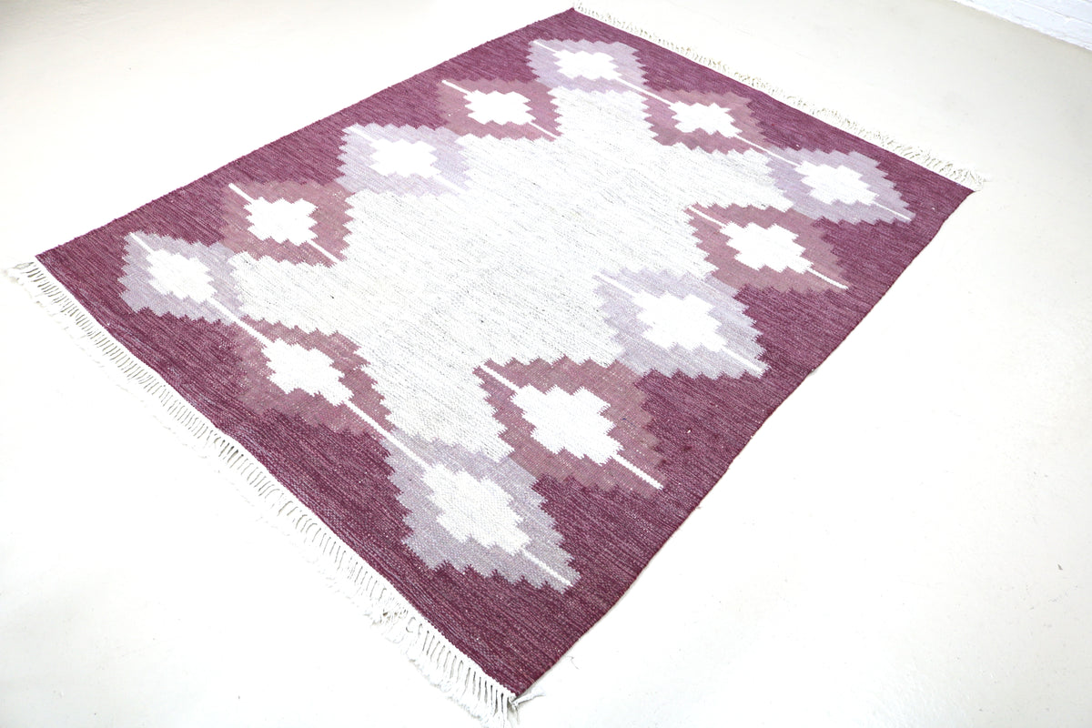 Angled view of Swedish Kilim rug featuring geometric diamond motifs in burgundy, ivory and grey