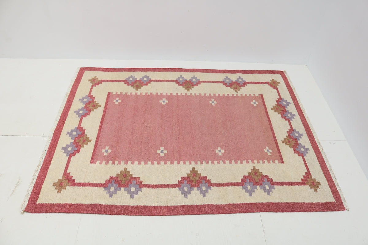 Angled view of Swedish Kilim rug featuring soft pink, ivory, lavender and brown modify