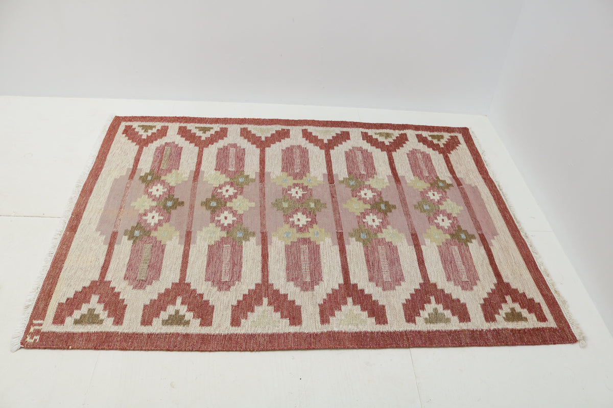 Angled view of Swedish Kilim rug featuring dusty rose, ivory and muted green motifs