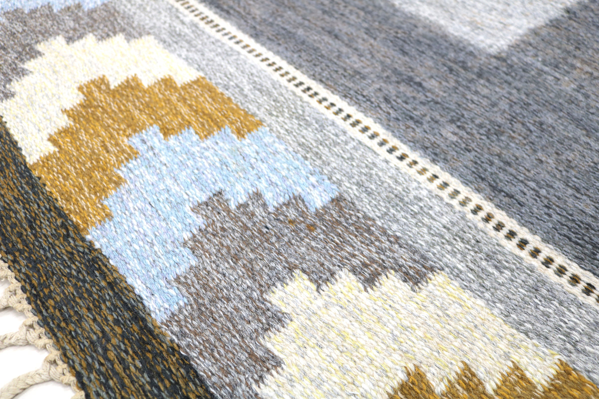 Detailed Swedish Kilim rug corner with geometric motifs in soft blue, warm ochre and grey