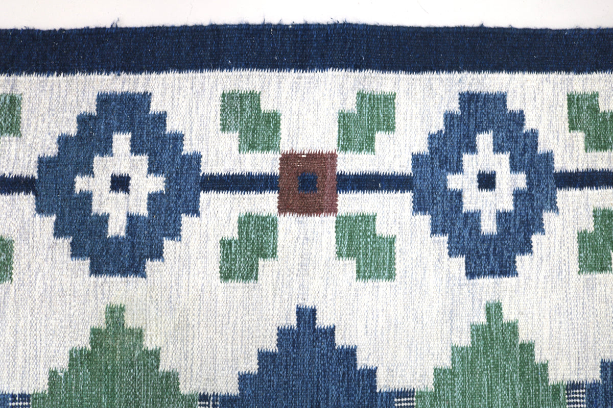 Vintage Swedish Kilim rug showing repeating floral motifs and geometric shapes in blue and green