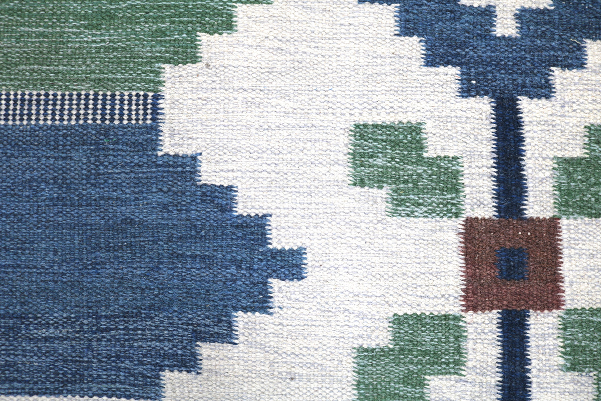 Detailed Swedish Kilim rug field featuring blue and green geometric shapes on an ivory background
