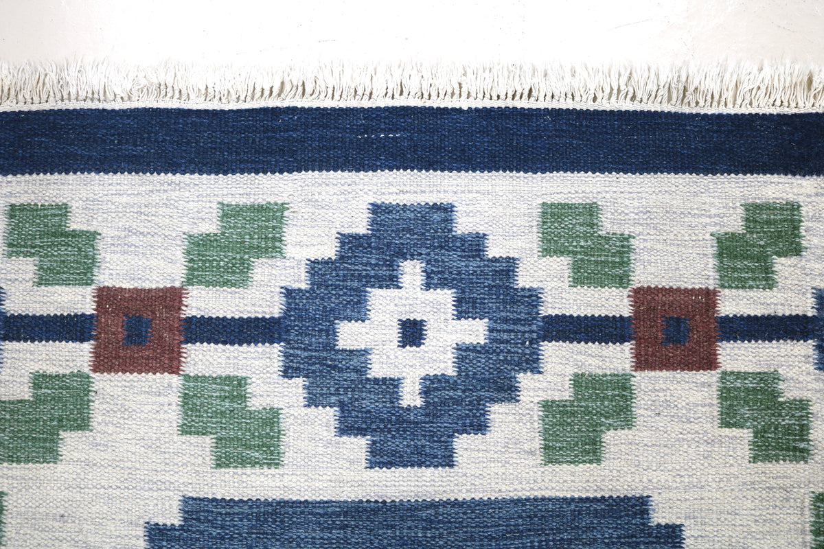 Close-up of Swedish Kilim rug border featuring geometric floral motifs in blue, green and ivory