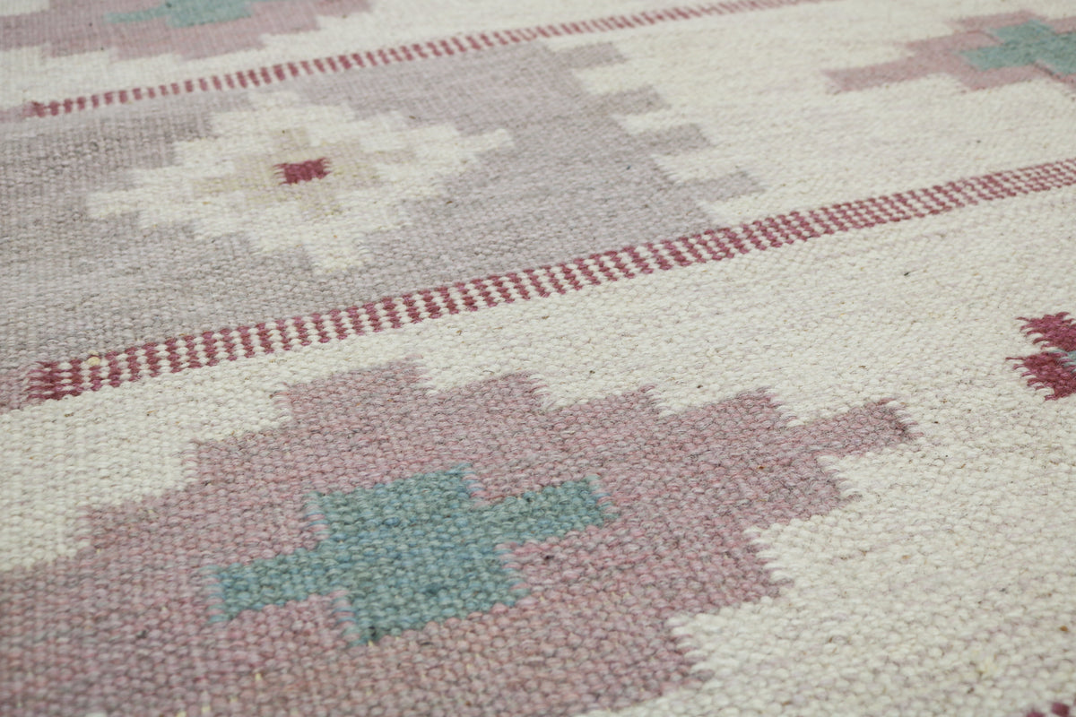 Close-up of Kilim rug featuring dusty pink geometric motifs on a cream field