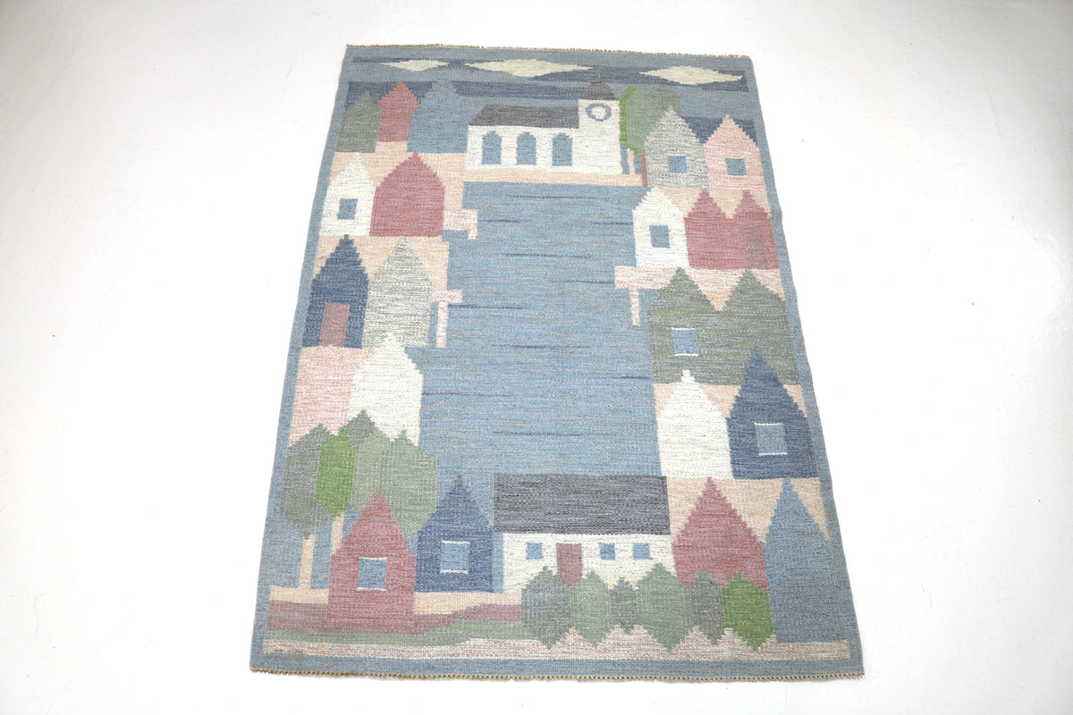 Full view of Swedish Kilim rug depicting houses, trees and rolling hills