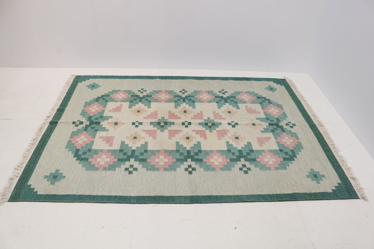 Angled view of Swedish Kilim rug featuring sage green, teal, dusty pink and ivory motifs
