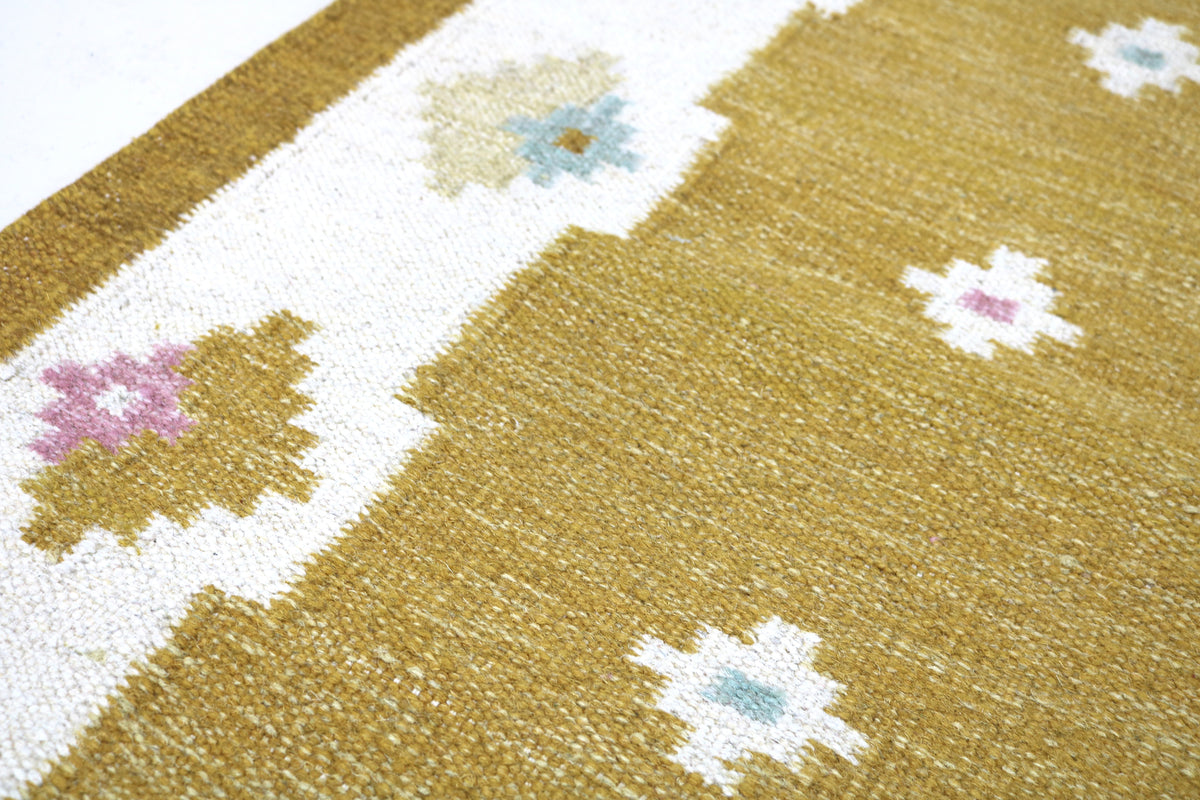 Close-up of Kilim runner showing pastel floral motifs against a golden ochre field