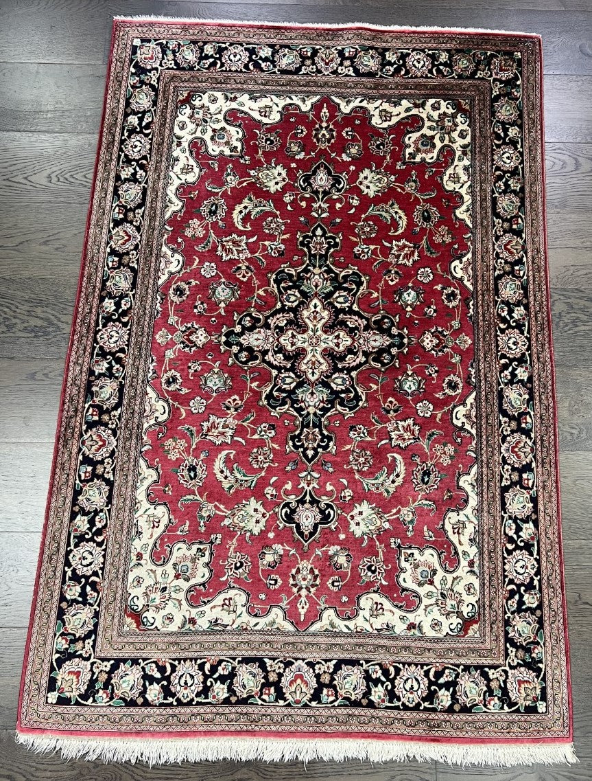 Full Isfahan silk rug showing central black floral medallion on a rich red field