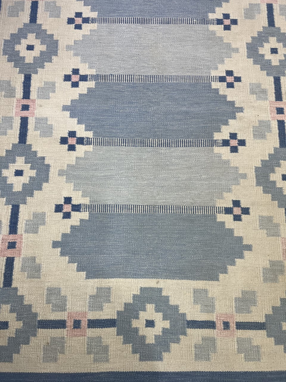 Close-up of geometric Kilim design with blue, cream and pink angular motifs