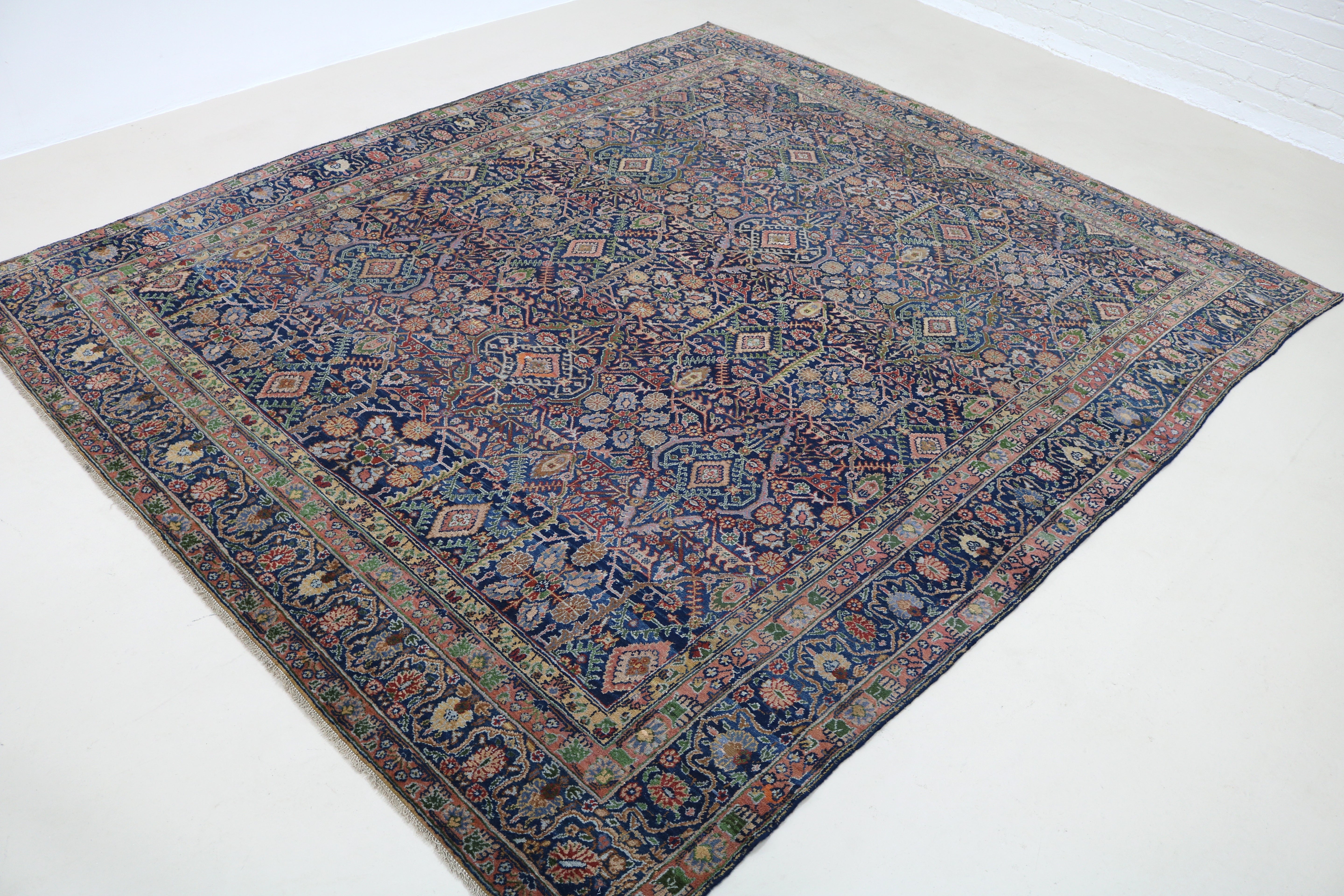 Angled view of antique Persian Senneh carpet showing detailed drawing and borders
