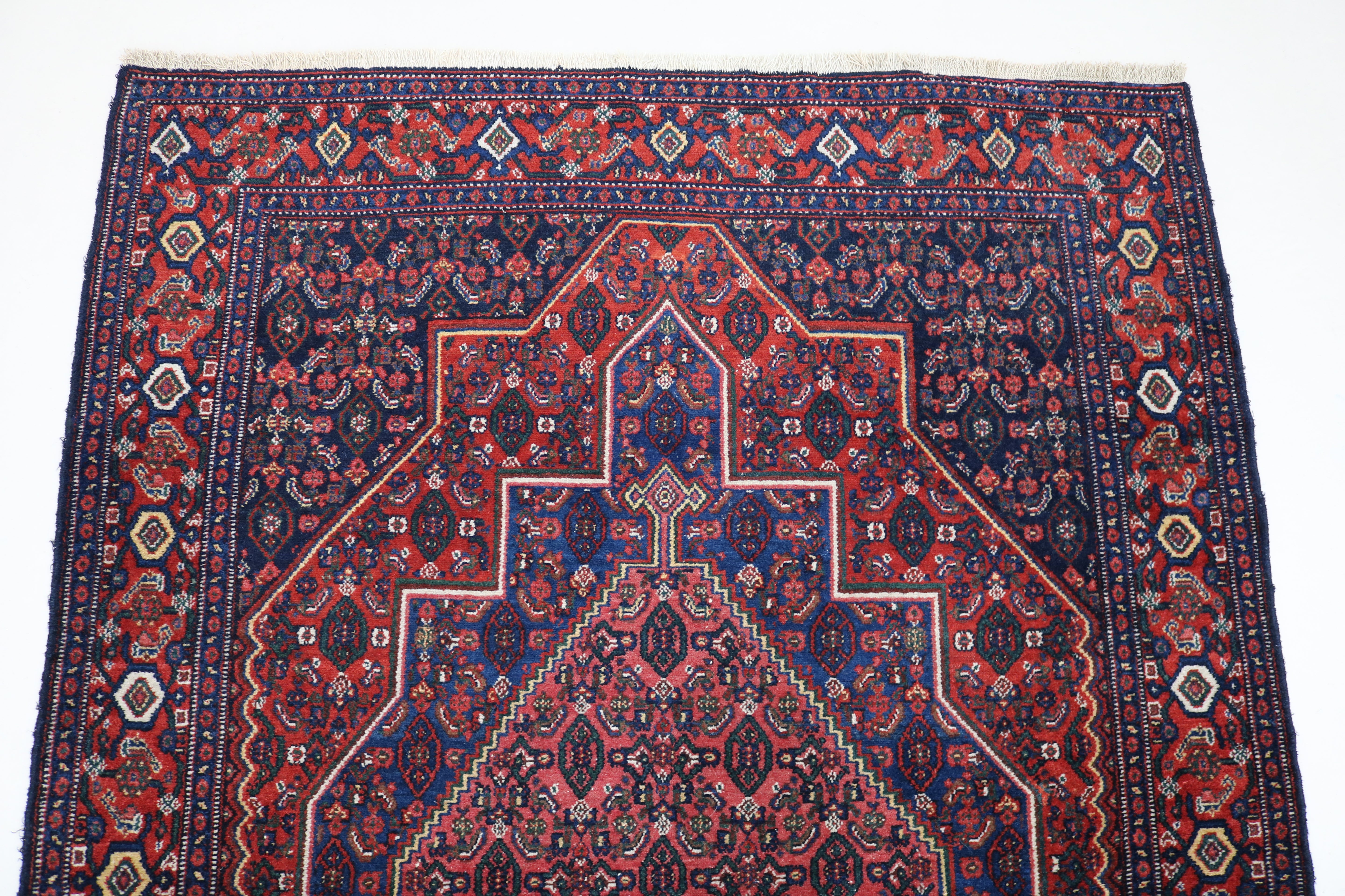 Angled view of antique Persian Senneh rug showing field and floral border
