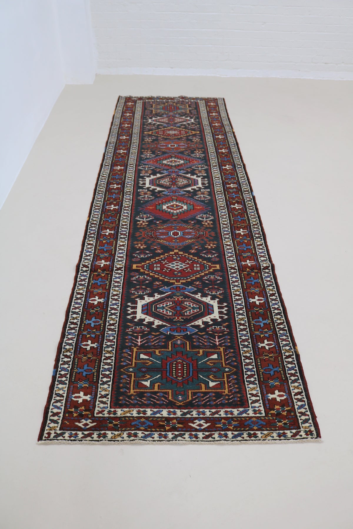Full view of antique Heriz runner with repeating geometric medallions and narrow format