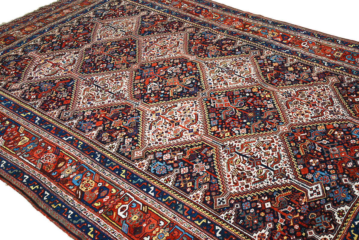 Detailed angled view of antique Qashqai carpet showing diamond motifs and deep indigo accents