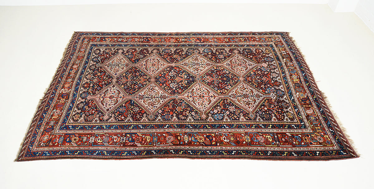 Angled view of Persian Qashqai carpet featuring geometric tribal motifs and richly patterned borders