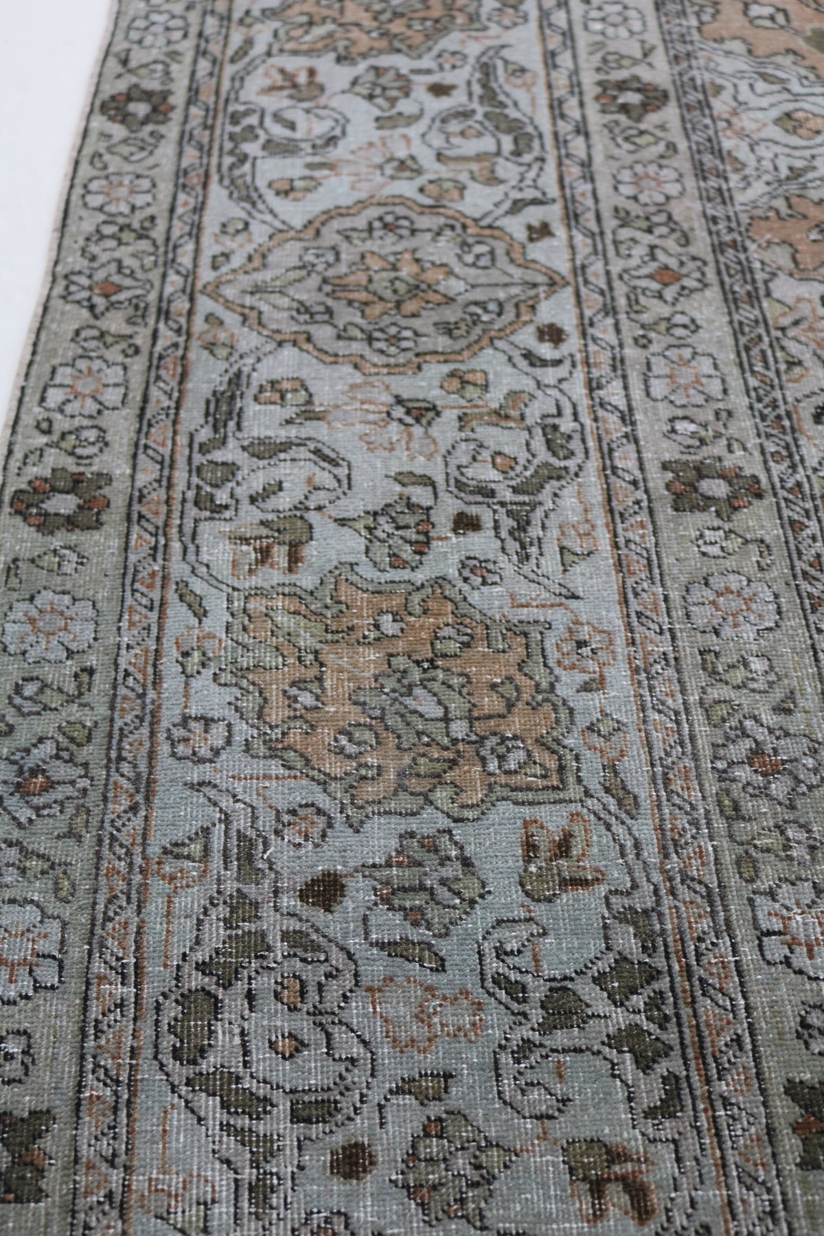 Close-up of Tabriz carpet showing delicate floral motifs on a warm beige field
