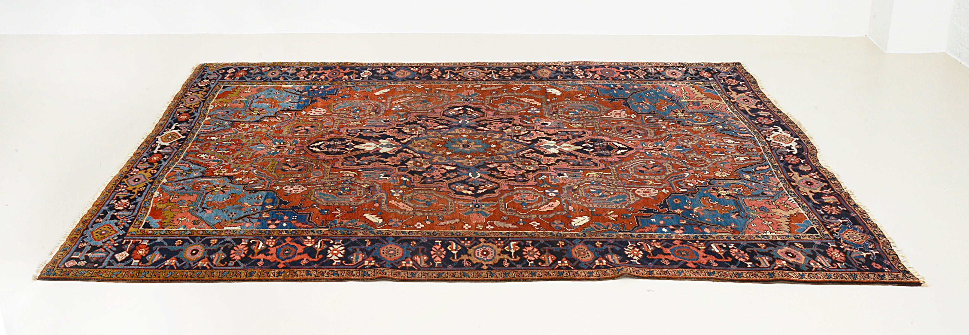 Angled view of antique Persian Heriz carpet showing field and borders
