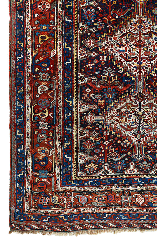 Corner view of an antique Persian Qashqai carpet showing tribal border and diamond lattice field details
