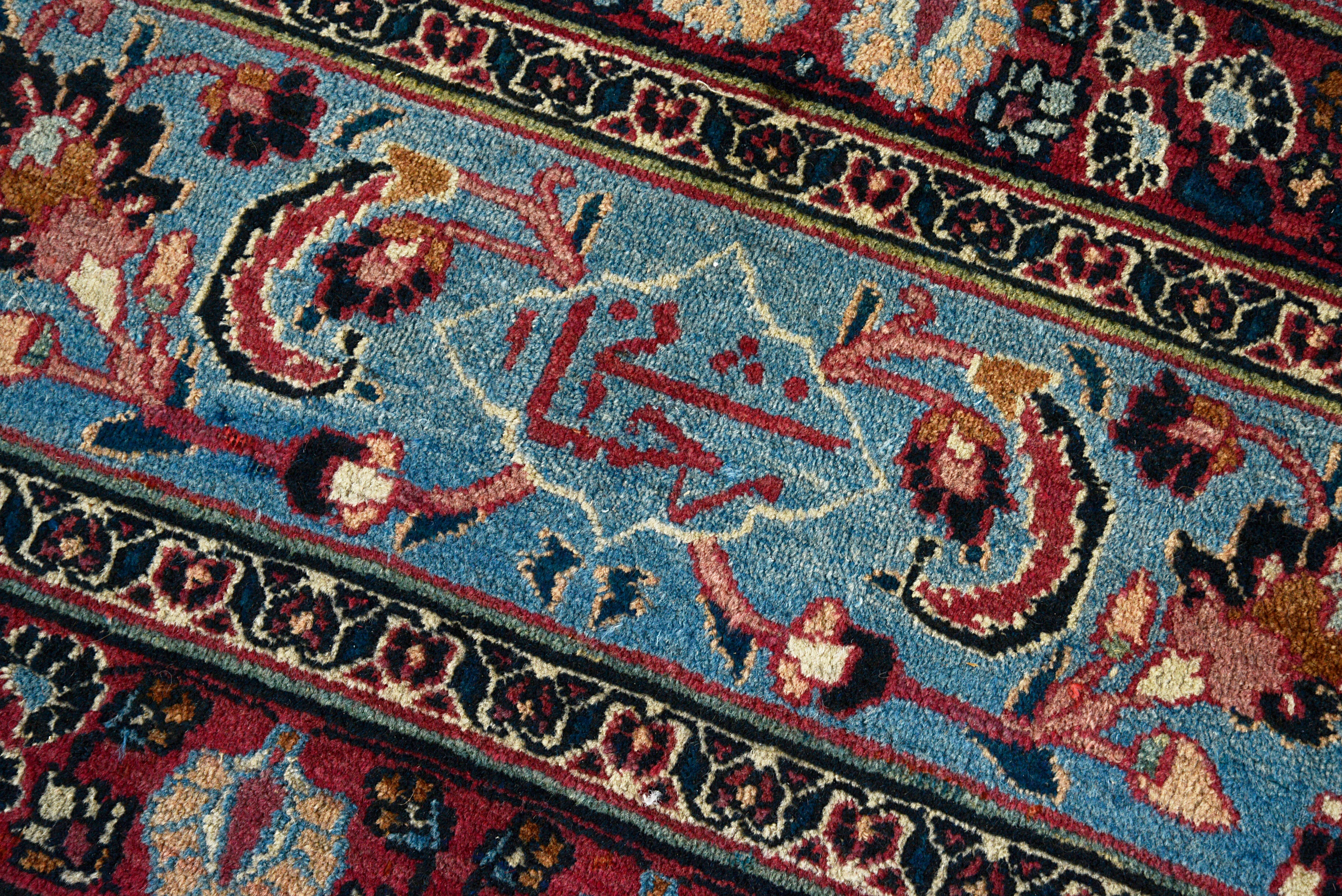 Close-up of deep blue, red, and ivory colours on an antique Persian Mashhad carpet
