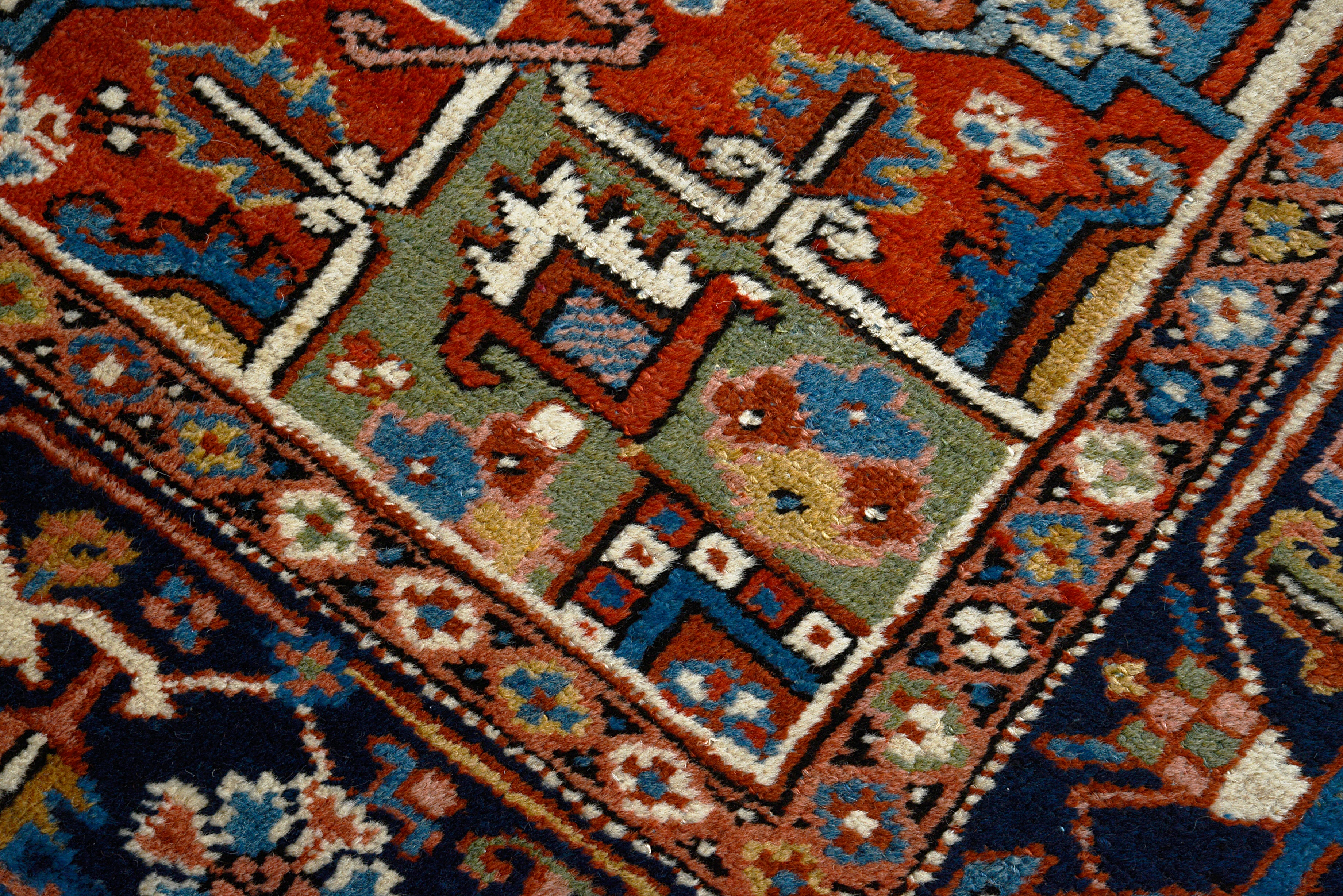 Close-up of terracotta, indigo, and ivory geometric patterns on an antique Persian Heriz carpet
