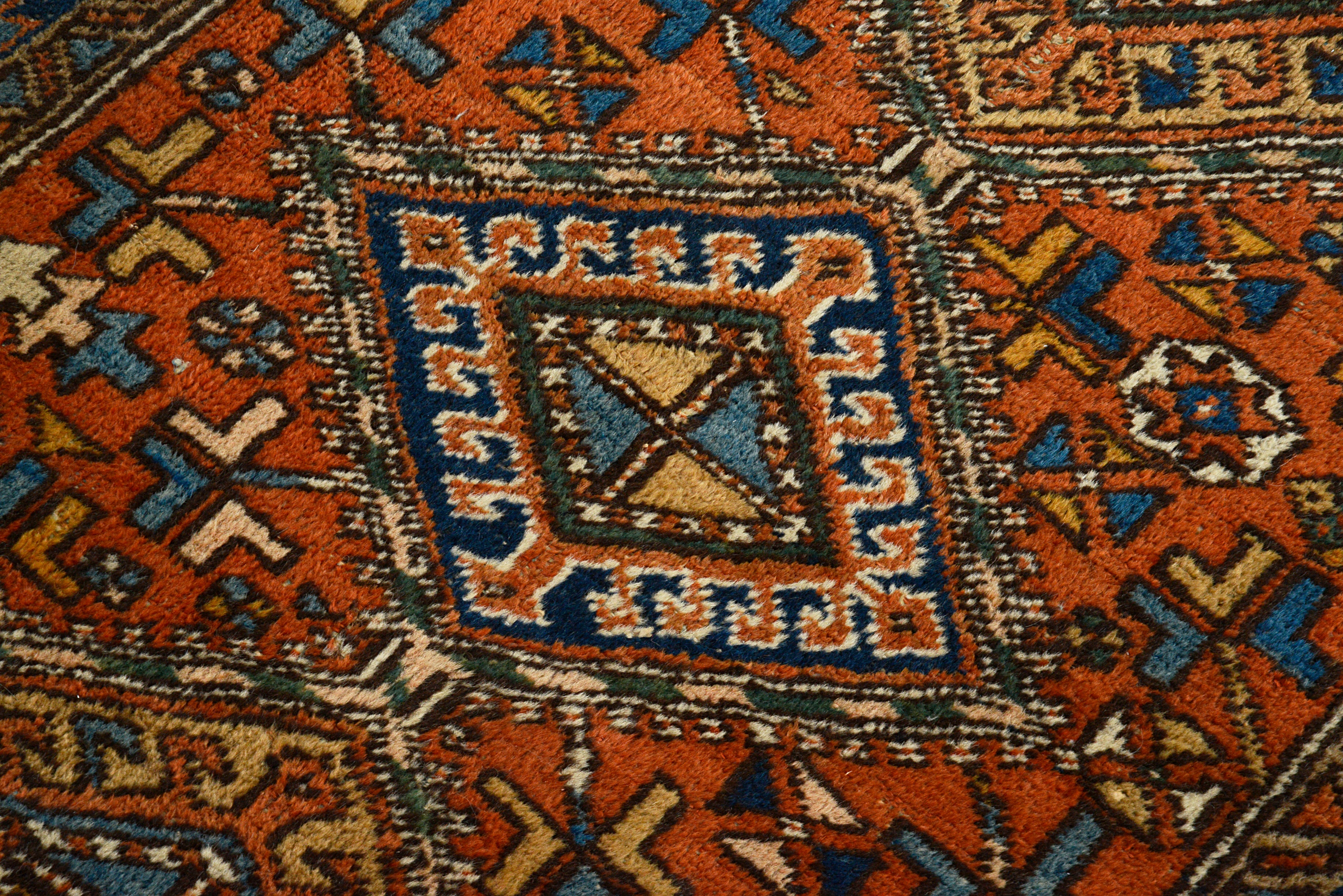 Close-up of a Oriental Antique rug with geometric designs in red, blue, and beige.