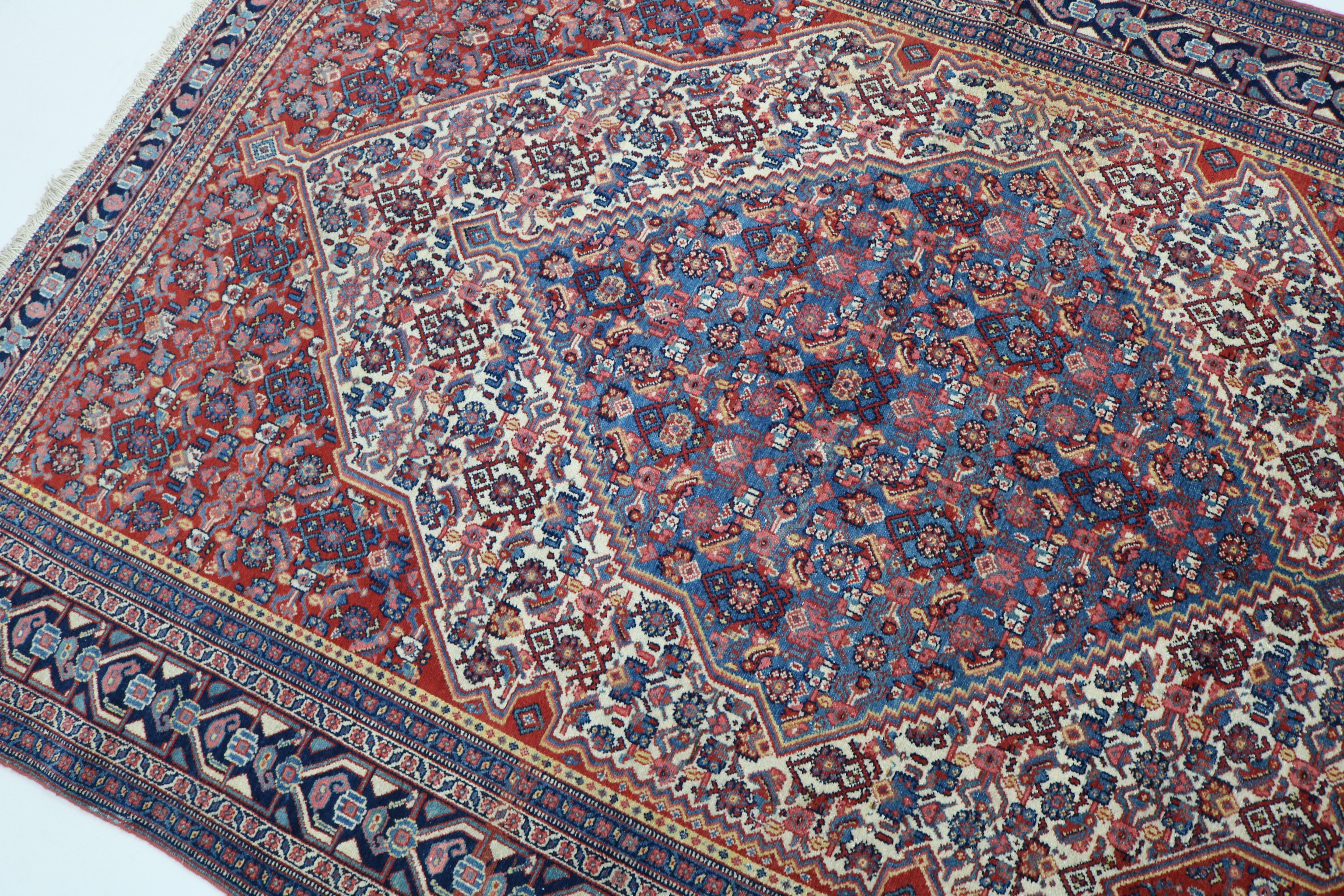 Angled view of antique Persian Senneh rug highlighting intricate design and borders
