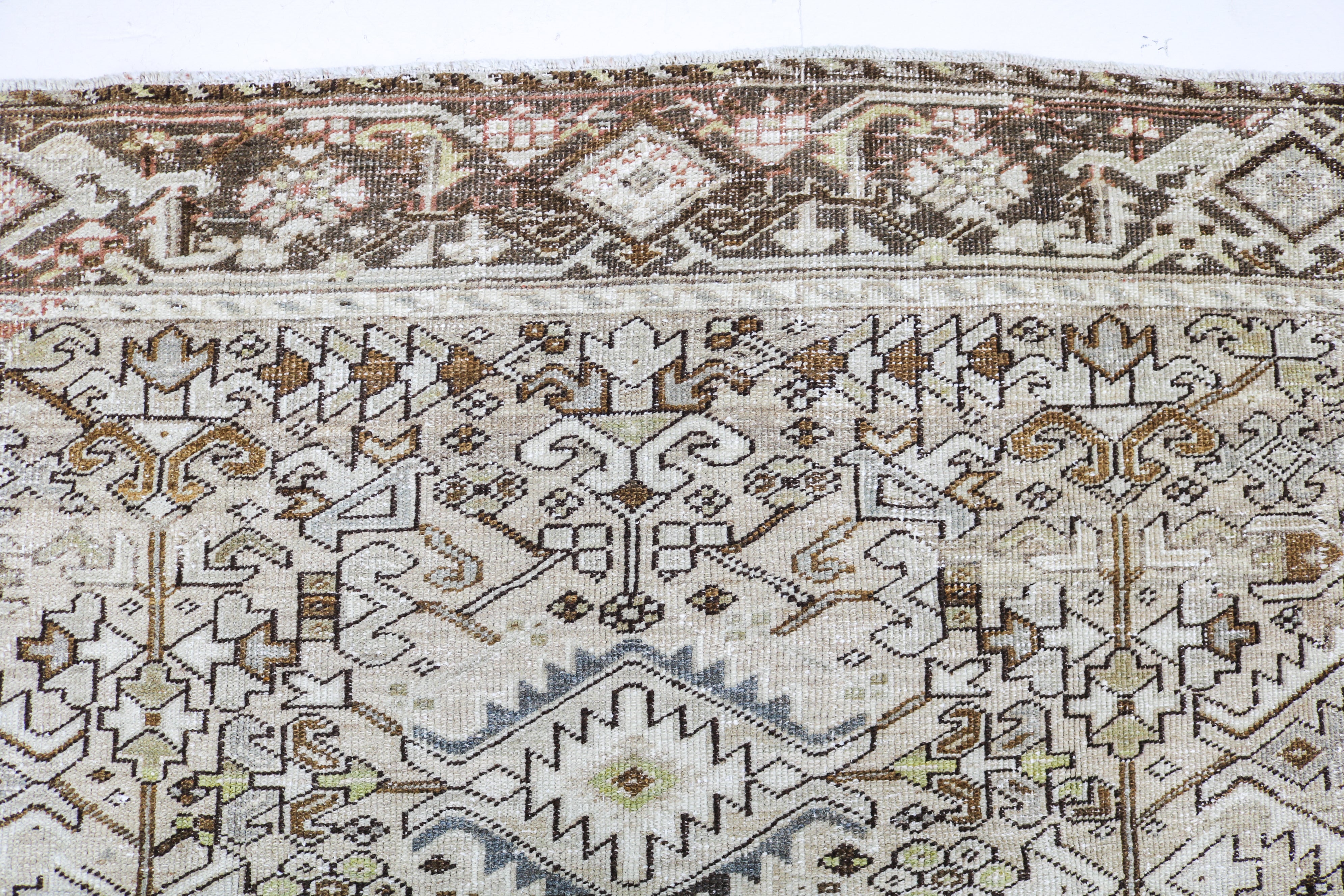 Detail of antique Persian Heriz carpet with geometric tribal motifs and softly faded natural tones