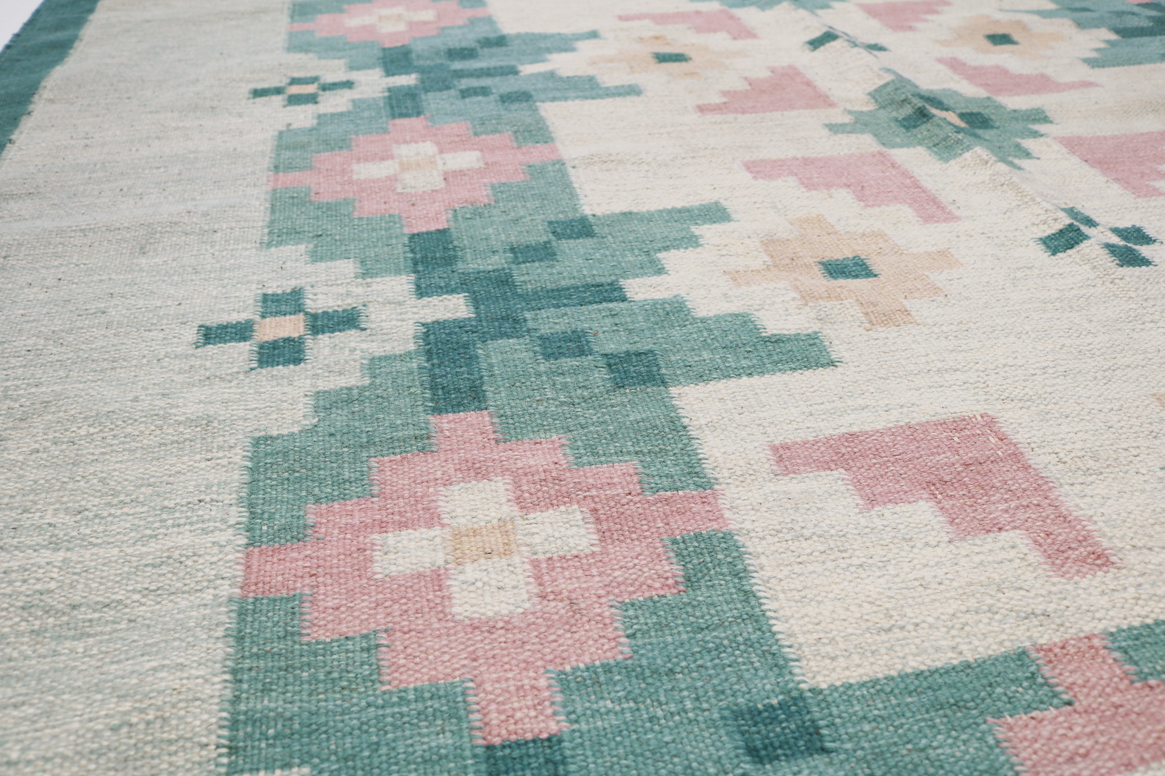 Close-up of vintage Swedish kilim showing green border, pink flower and handwoven wool texture 6