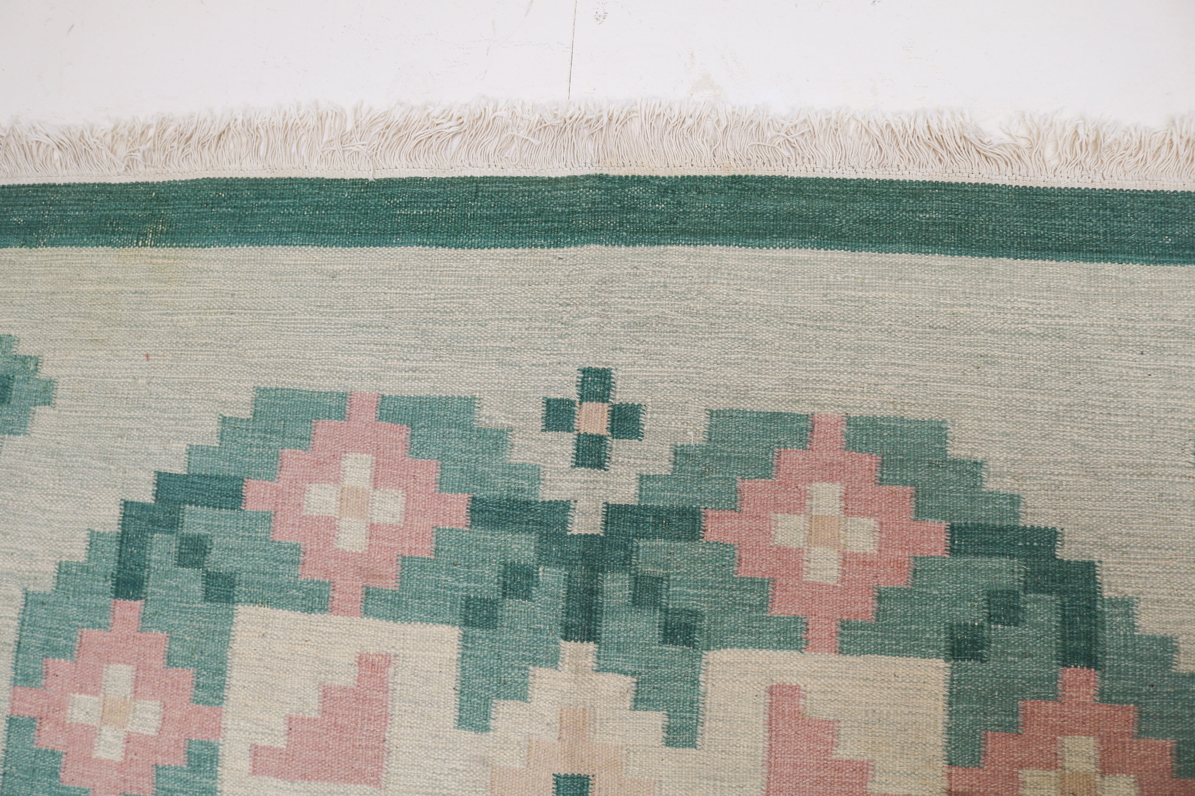 Close-up of vintage Swedish kilim showing green border, pink flower and handwoven wool texture 8