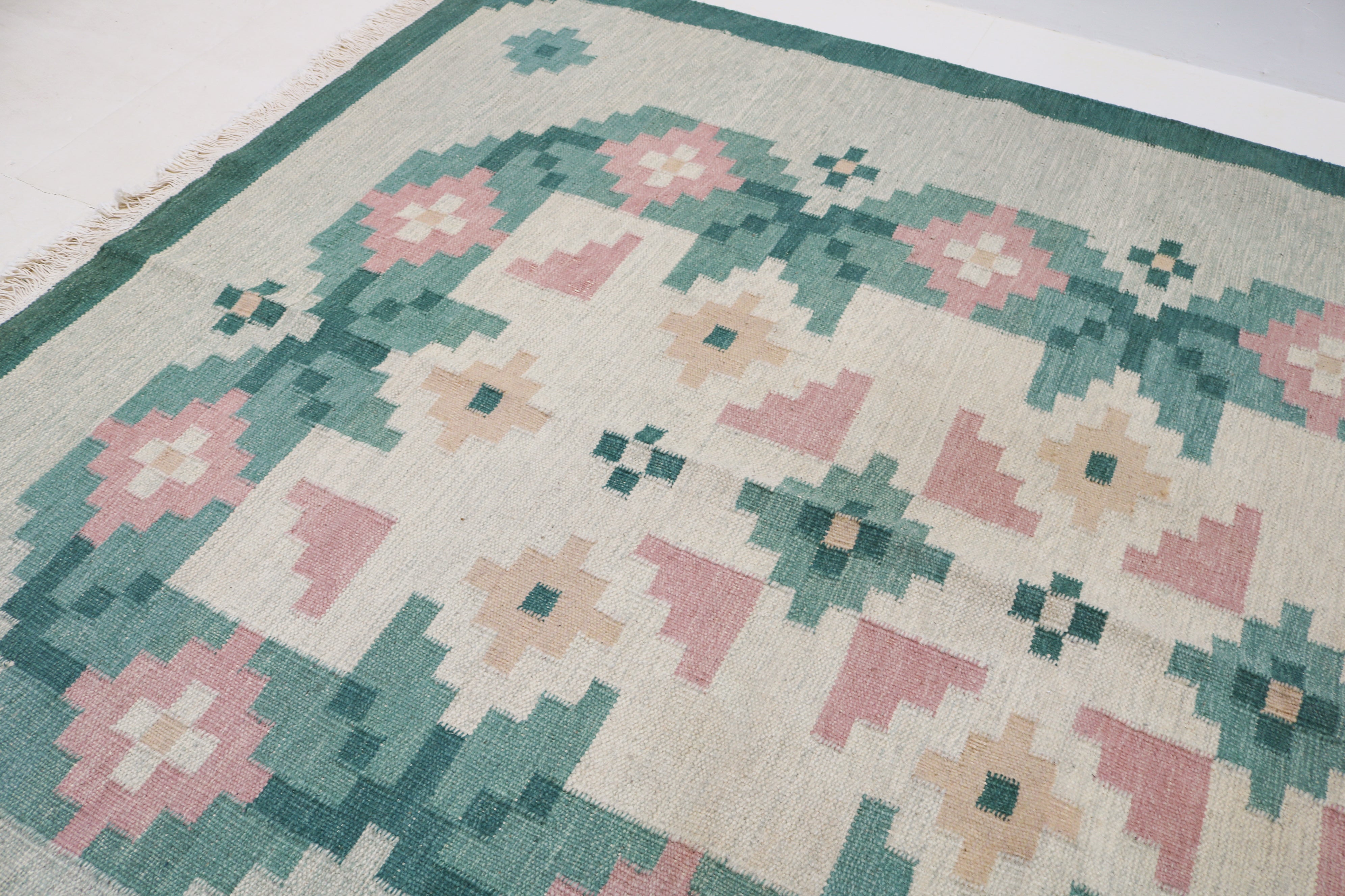 Close-up of vintage Swedish kilim showing green border, pink flower and handwoven wool texture 9