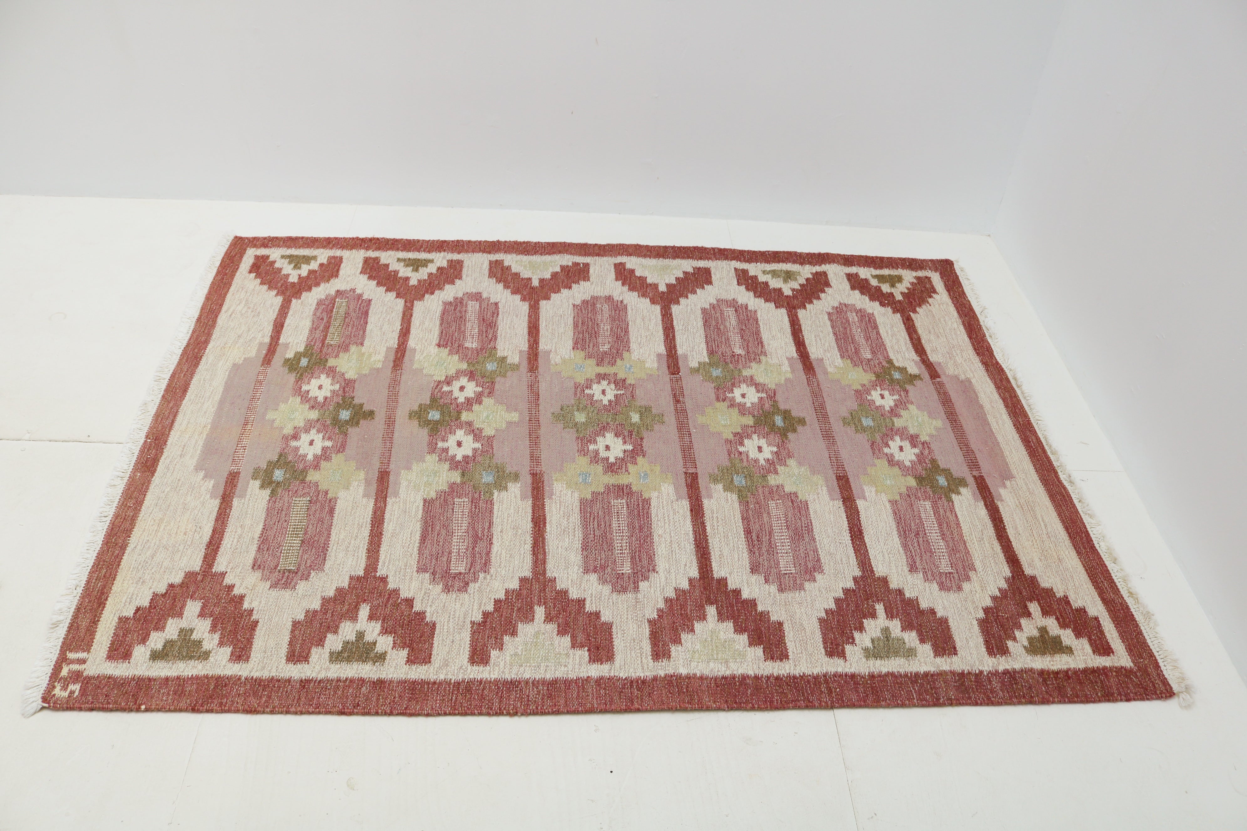 Close-up of handwoven vintage Swedish kilim with geometric floral motifs in dusty pink, green and ivory