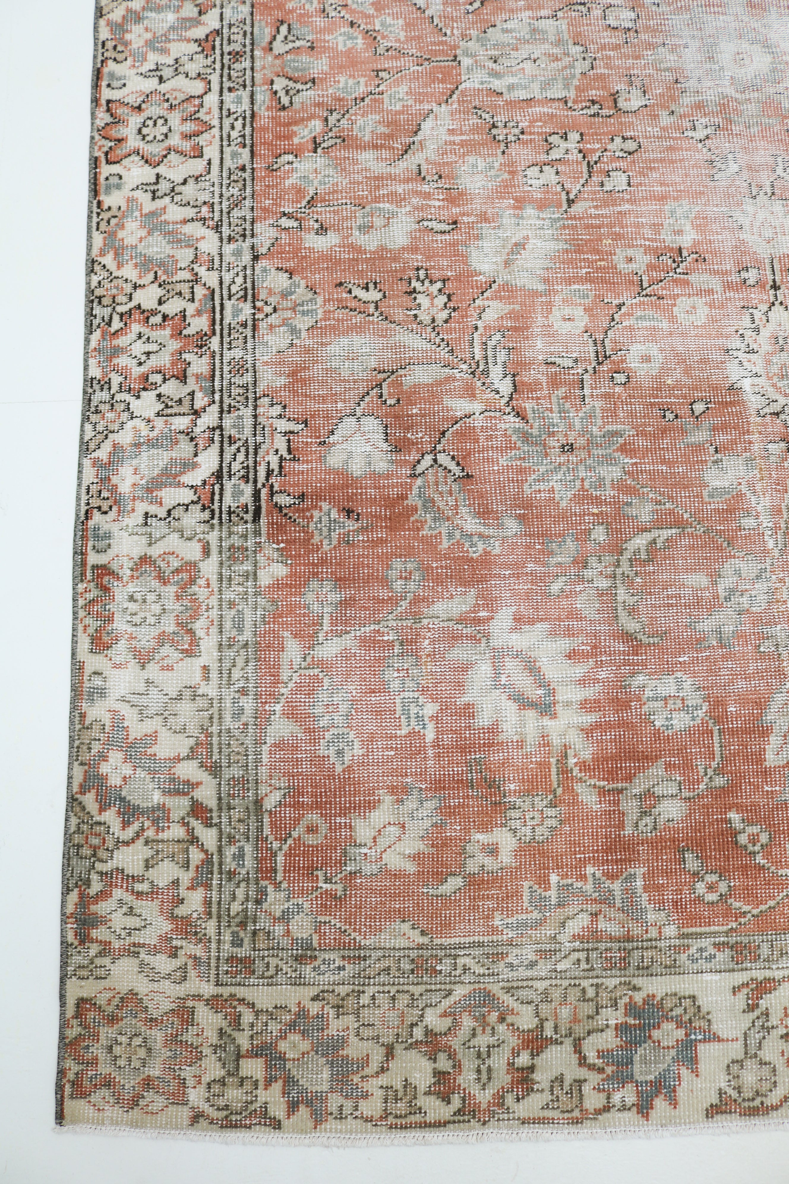 Close-up of vintage Turkish rug showing faded terracotta, ivory and pale grey floral motifs with naturally worn wool pile
