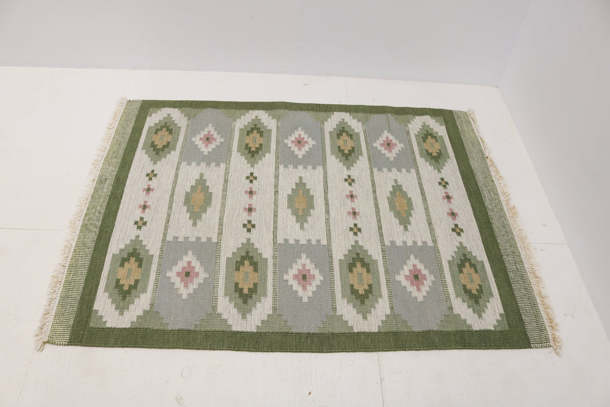 Angled view of Swedish Kilim rug featuring olive green, ivory, beige and dusty pink motif