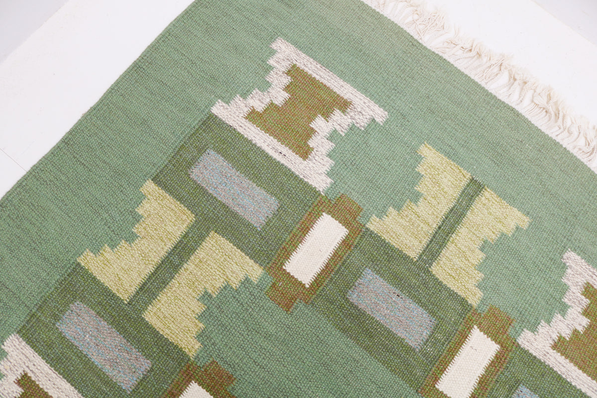 Detailed Swedish Kilim rug showing repeating abstract geometric shapes across the green field
