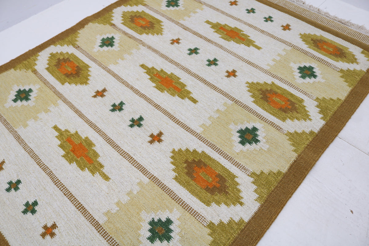 Angled view of vintage Swedish Kilim rug with repeating geometric medallions and muted colours
