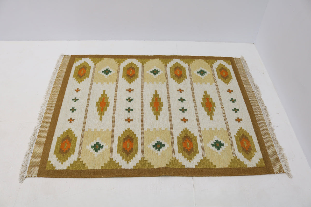 Angled view of Swedish Kilim rug featuring ochre, olive green and burnt orange motifs