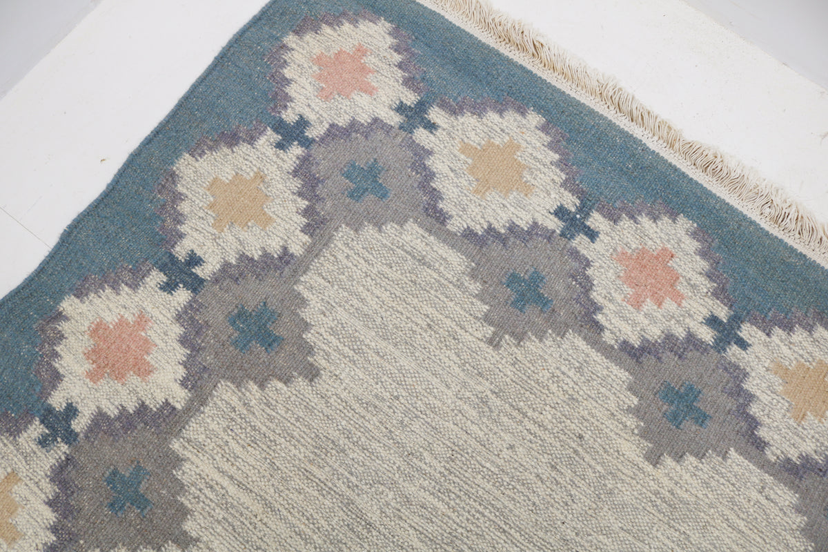 Detailed Swedish Kilim rug corner featuring geometric floral motifs in muted Scandinavian colours
