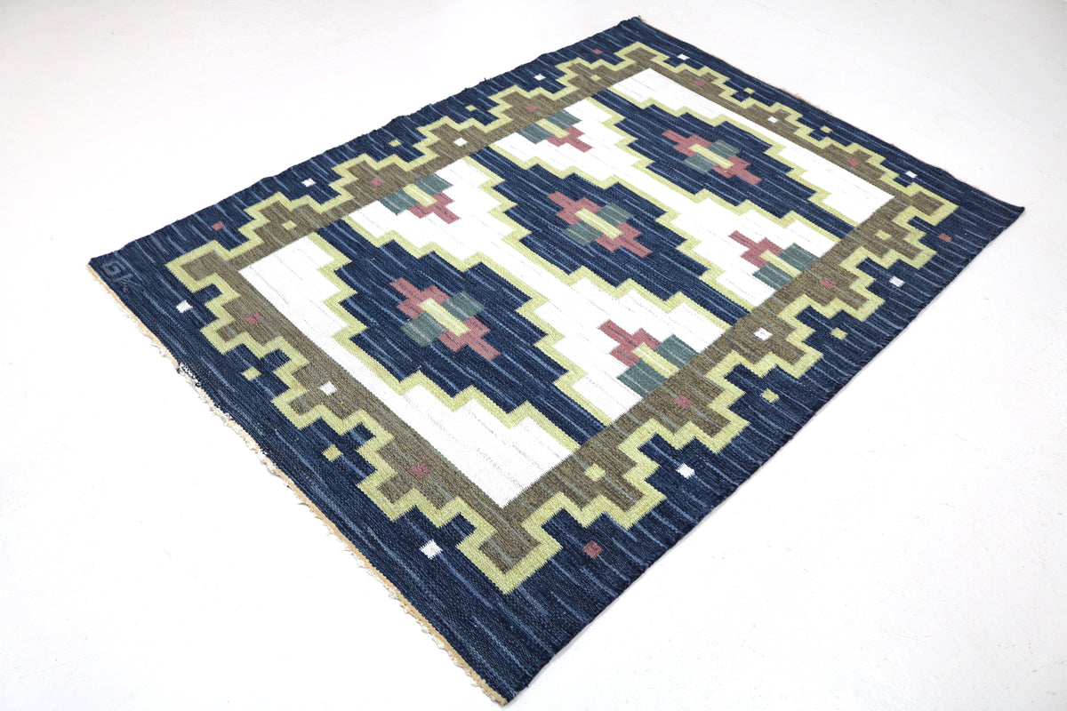 Angled view of Swedish Kilim rug featuring navy, ivory, olive green and pink geometric designs