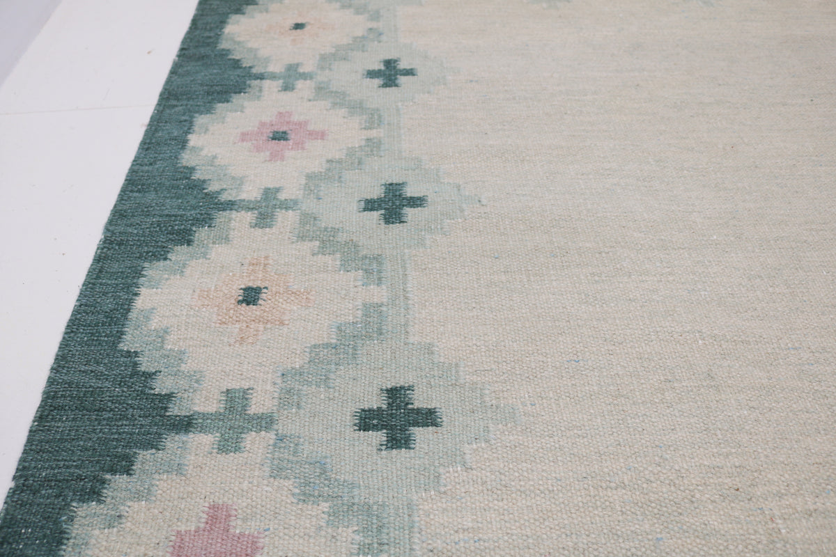 Detailed view of Swedish Kilim rug with repeating floral motifs in muted teal and ivory
