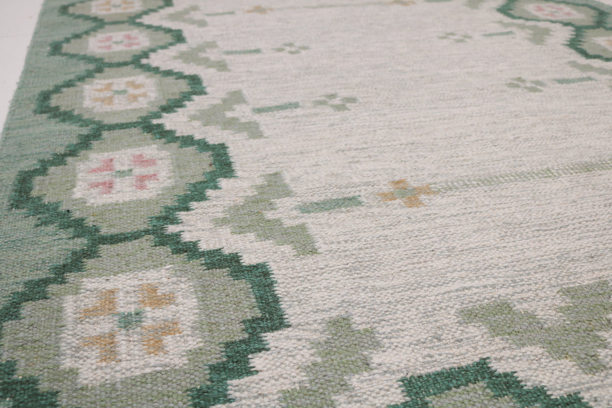 Detailed Swedish Kilim rug showing geometric floral motifs across the pale grey field