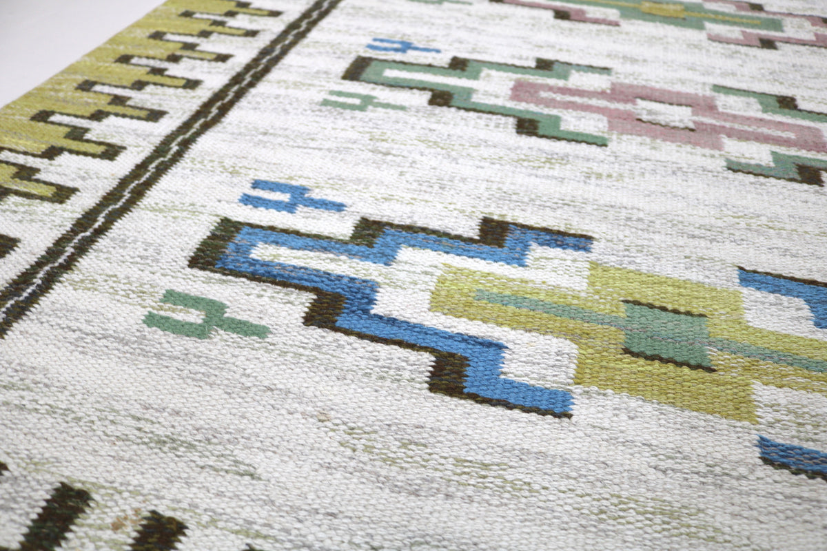 Close-up of Kilim rug featuring blue, green and pink geometric motifs on ivory
